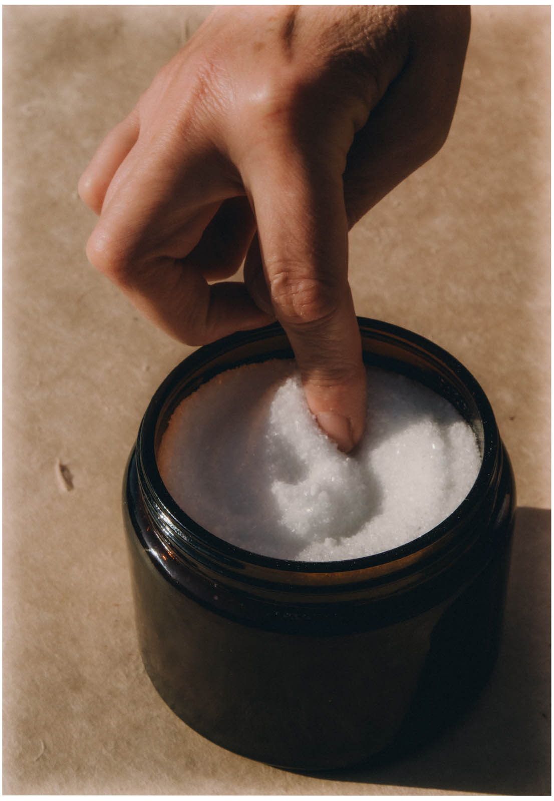 A finger lifting sea salt from an amber jar